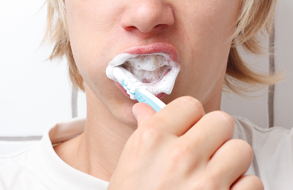Person brushing teeth with a blue toothbrush, white toothpaste foam visible