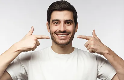 Man in a white shirt smiling and pointing at his teeth with both index fingers