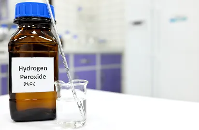 Brown bottle labeled "Hydrogen Peroxide" beside a clear beaker with liquid and a pipette in a bright